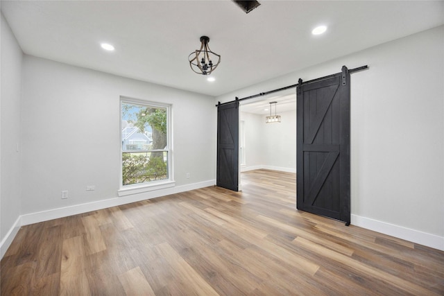 empty room with a barn door, wood finished floors, baseboards, and recessed lighting