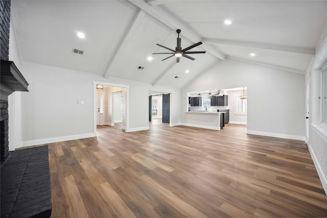 unfurnished living room featuring visible vents, ceiling fan with notable chandelier, beamed ceiling, wood finished floors, and a brick fireplace