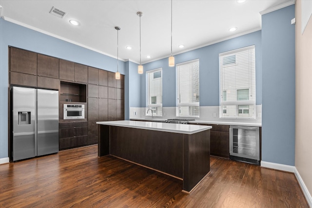 kitchen featuring ornamental molding, appliances with stainless steel finishes, dark brown cabinetry, wine cooler, and a kitchen island