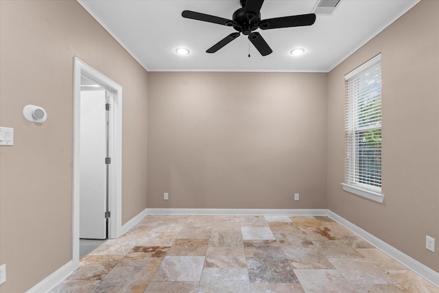 empty room with stone tile floors, a ceiling fan, ornamental molding, visible vents, and baseboards