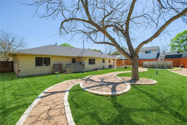 back of house featuring brick siding, a fenced backyard, a swimming pool, and a yard