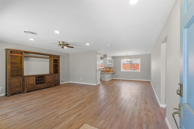 unfurnished living room featuring ceiling fan with notable chandelier, visible vents, light wood-style flooring, and baseboards