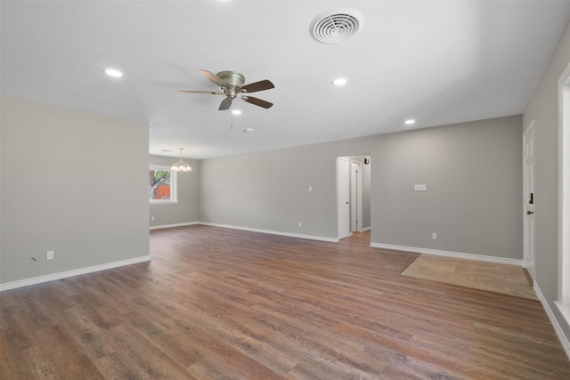 empty room with baseboards, visible vents, ceiling fan with notable chandelier, and wood finished floors