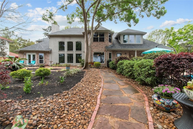 rear view of property with roof with shingles, a chimney, and brick siding