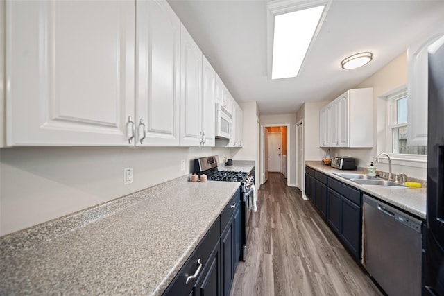 kitchen featuring light countertops, stainless steel appliances, white cabinetry, a sink, and light wood-type flooring