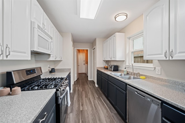 kitchen featuring light countertops, light wood finished floors, appliances with stainless steel finishes, white cabinetry, and a sink