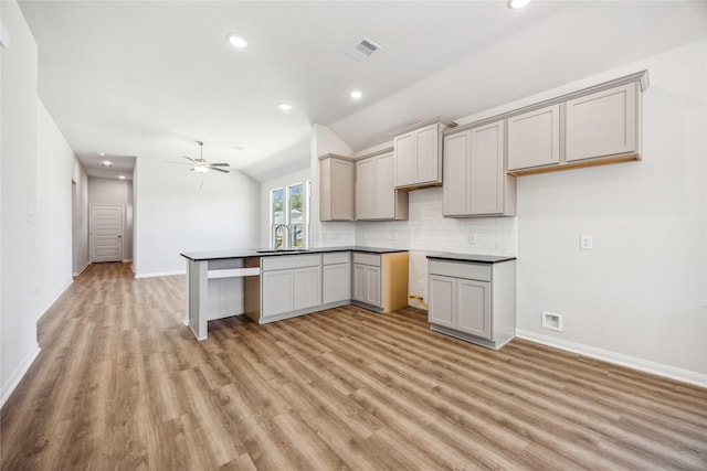 kitchen featuring decorative backsplash, vaulted ceiling, light wood finished floors, a sink, and baseboards