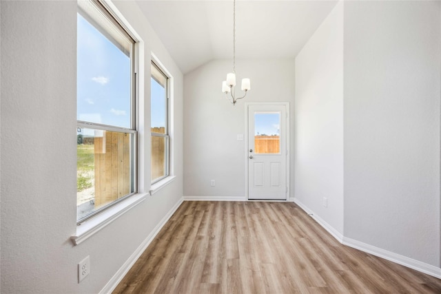 unfurnished dining area with wood finished floors, a chandelier, vaulted ceiling, and baseboards