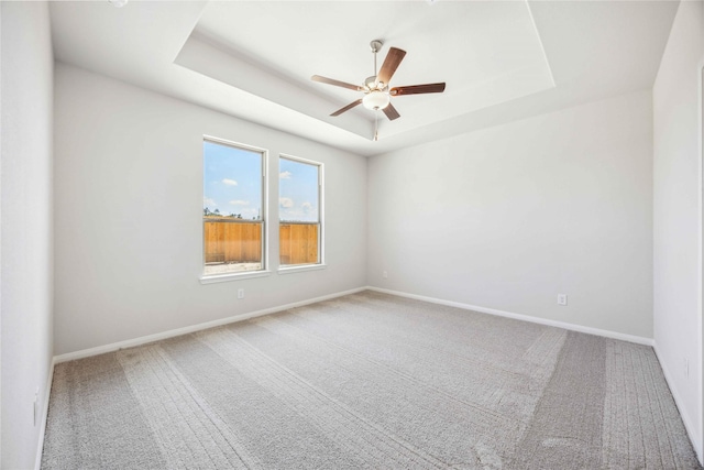 carpeted empty room featuring a ceiling fan, baseboards, and a tray ceiling