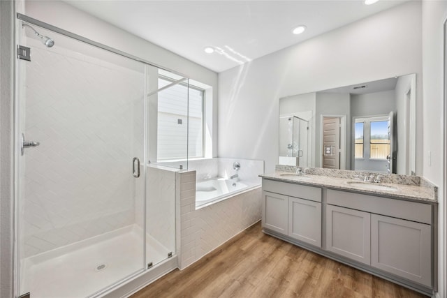full bath with wood finished floors, a shower stall, double vanity, a sink, and a garden tub