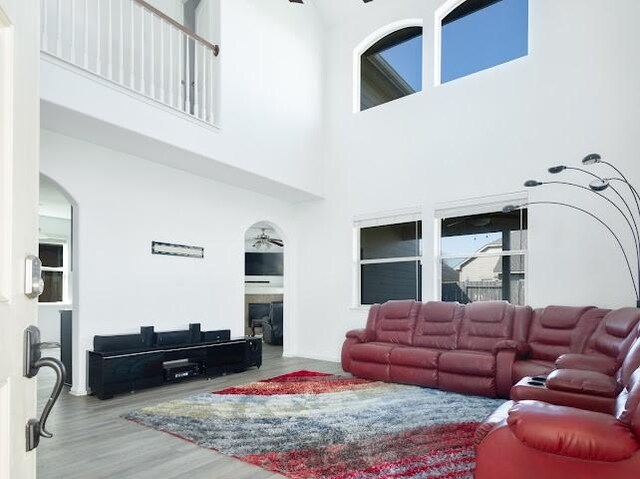 living area with a fireplace, a high ceiling, wood finished floors, arched walkways, and ceiling fan