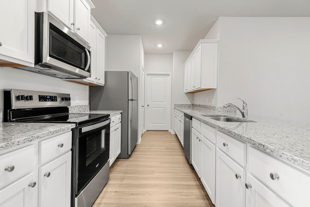 kitchen with light stone counters, stainless steel appliances, light wood-style floors, white cabinets, and a sink