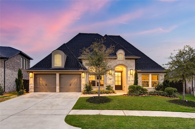 french provincial home with a garage, a lawn, brick siding, roof with shingles, and driveway