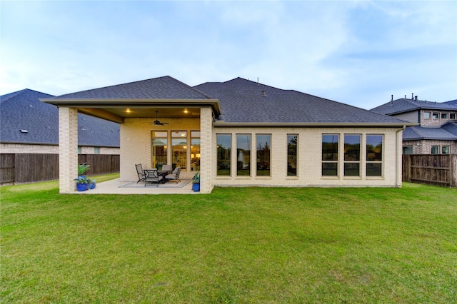rear view of property featuring a ceiling fan, a fenced backyard, brick siding, and a lawn