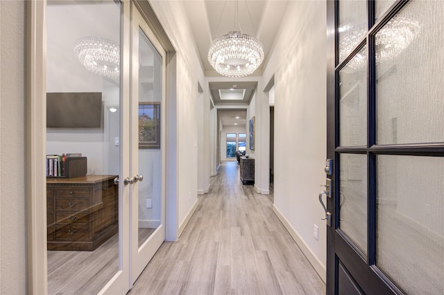 corridor with baseboards, french doors, light wood-style flooring, and a chandelier