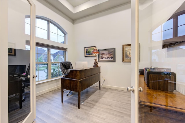 office area with a towering ceiling, baseboards, and light wood-type flooring
