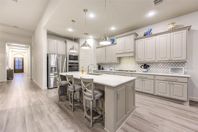 kitchen with a breakfast bar, appliances with stainless steel finishes, light wood-style flooring, visible vents, and decorative backsplash