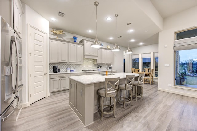 kitchen with tasteful backsplash, a sink, light wood finished floors, visible vents, and appliances with stainless steel finishes