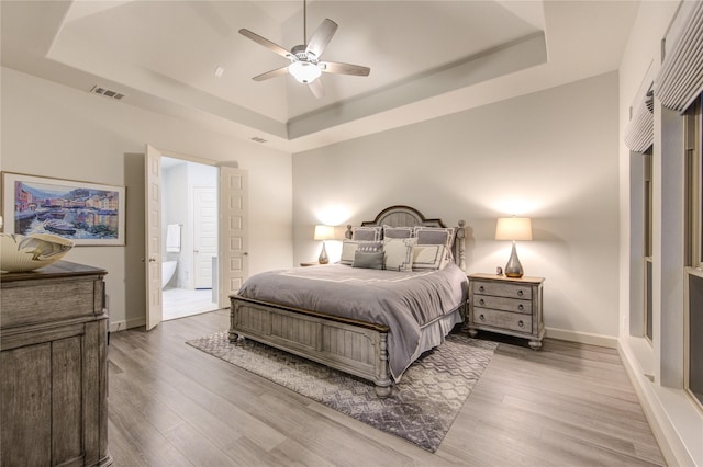 bedroom featuring light wood-type flooring, a raised ceiling, and visible vents