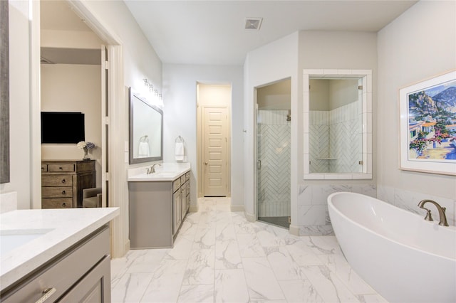 full bath featuring marble finish floor, two vanities, a sink, a stall shower, and a freestanding bath