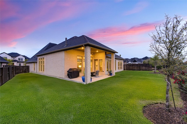 rear view of house featuring a fenced backyard, a patio, brick siding, and a lawn