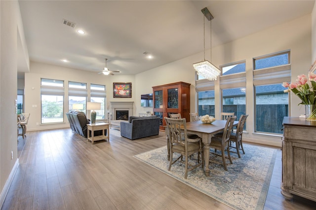 dining space featuring a fireplace, visible vents, ceiling fan with notable chandelier, and wood finished floors