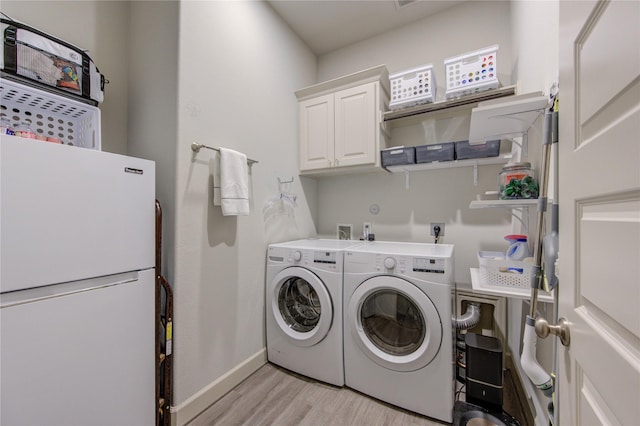clothes washing area featuring light wood finished floors, baseboards, washer and dryer, and cabinet space
