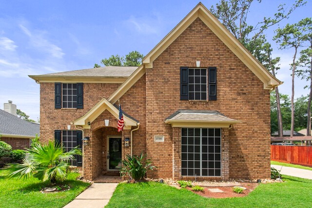 traditional-style house featuring fence, a front lawn, and brick siding