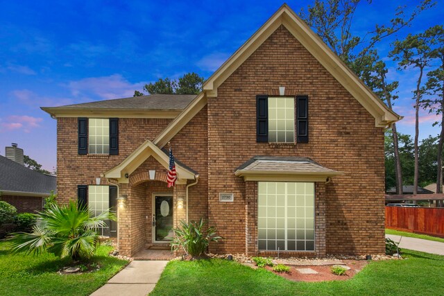 traditional home featuring a lawn, fence, and brick siding