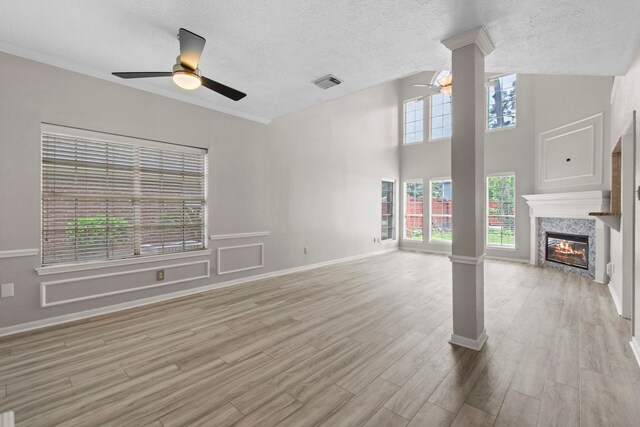 unfurnished living room with a ceiling fan, visible vents, a tiled fireplace, wood finished floors, and ornate columns