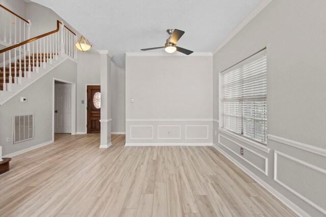 unfurnished living room featuring ceiling fan, visible vents, wood finished floors, stairway, and ornamental molding