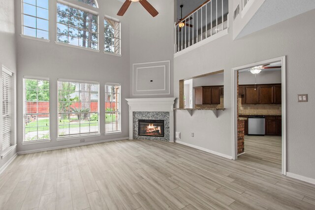 unfurnished living room featuring ceiling fan, light wood finished floors, and a high ceiling