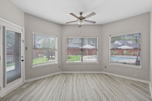 empty room with baseboards, ceiling fan, a healthy amount of sunlight, and light wood-style floors