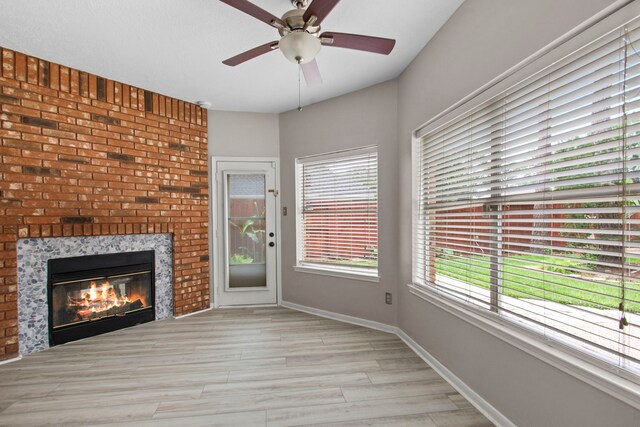 unfurnished living room featuring a fireplace, ceiling fan, baseboards, and light wood-type flooring