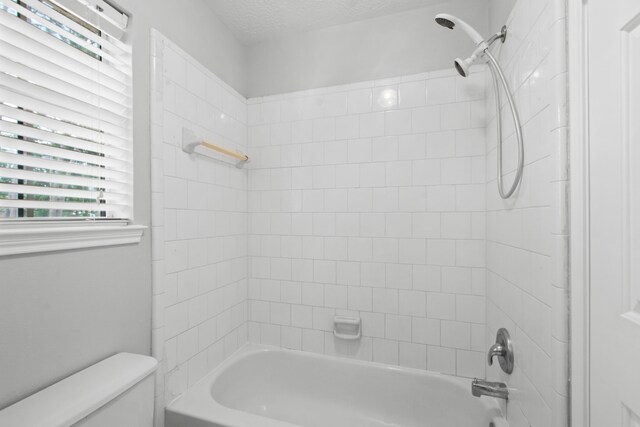 full bathroom with washtub / shower combination, toilet, and a textured ceiling