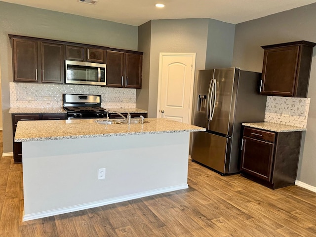 kitchen featuring a sink, light wood-style flooring, light stone countertops, dark brown cabinetry, and appliances with stainless steel finishes