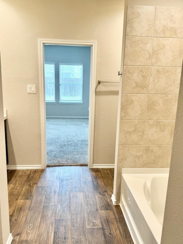 bathroom featuring a tub, baseboards, wood finished floors, and a textured wall