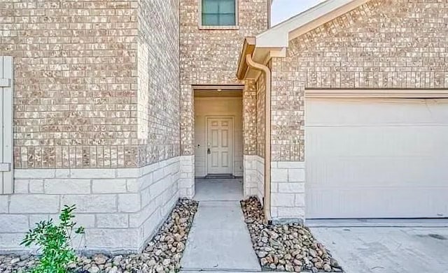 view of exterior entry with an attached garage and brick siding