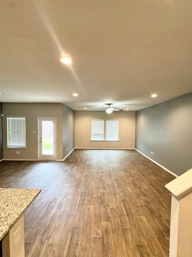 unfurnished living room with baseboards, a textured ceiling, wood finished floors, and a ceiling fan