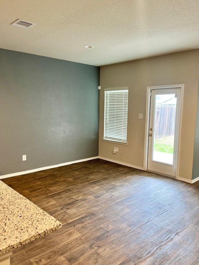 empty room featuring baseboards, a textured ceiling, dark wood-style floors, and visible vents