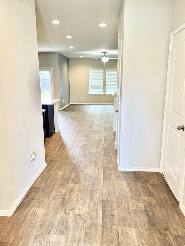 hall featuring baseboards, wood finished floors, and recessed lighting