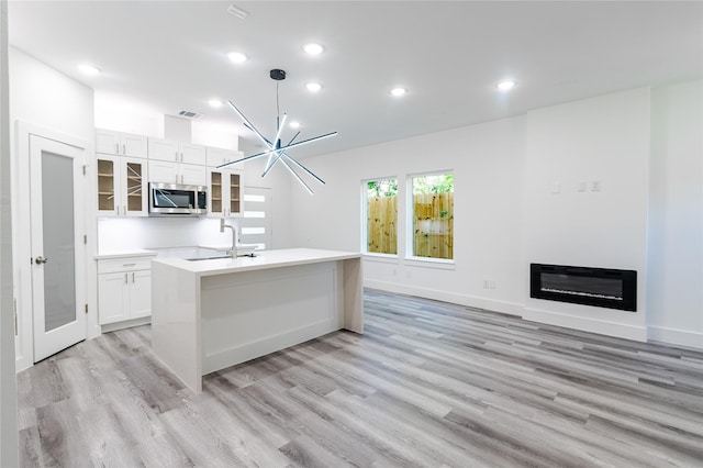 5304 Lynnfield St, Houston, TX 77028 - kitchen with stainless steel microwave, an island with sink, light wood-style floors, white cabinetry, and glass insert cabinets