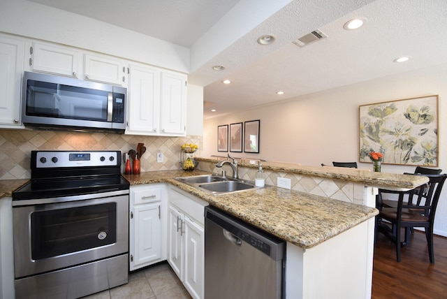 kitchen with white cabinetry, a sink, visible vents, a peninsula, and appliances with stainless steel finishes