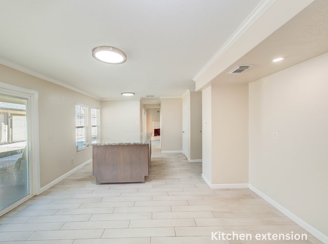 kitchen featuring baseboards, visible vents, light stone counters, a kitchen island, and ornamental molding