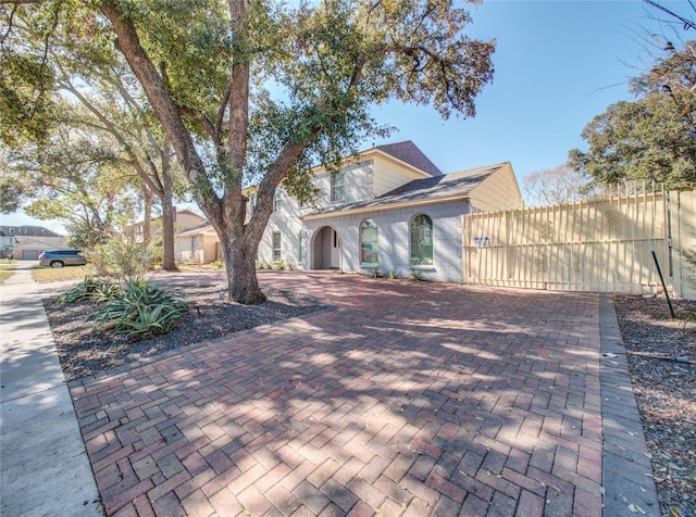 view of front of home featuring a gate, brick siding, decorative driveway, and roof with shingles