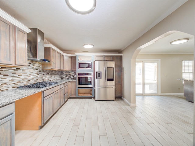 kitchen with stainless steel appliances, arched walkways, wall chimney exhaust hood, crown molding, and tasteful backsplash