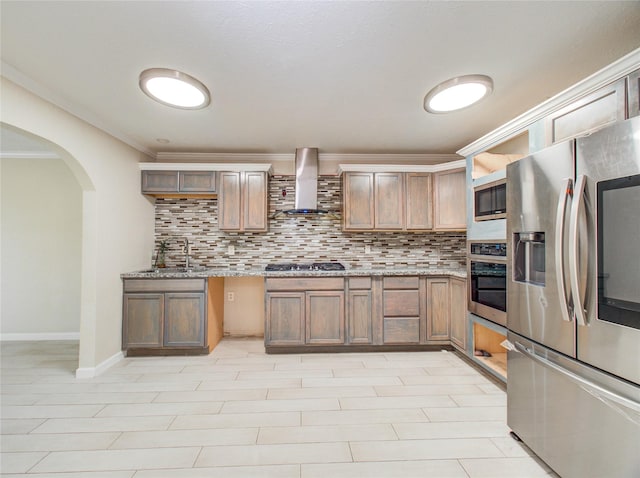 kitchen featuring wall chimney range hood, crown molding, arched walkways, stainless steel appliances, and backsplash