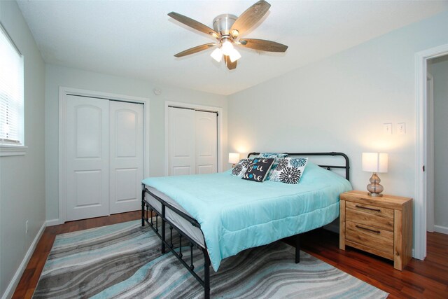 bedroom with two closets, wood finished floors, baseboards, and ceiling fan