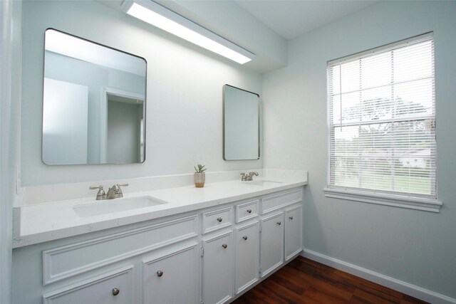 full bath with wood finished floors, plenty of natural light, baseboards, and double vanity