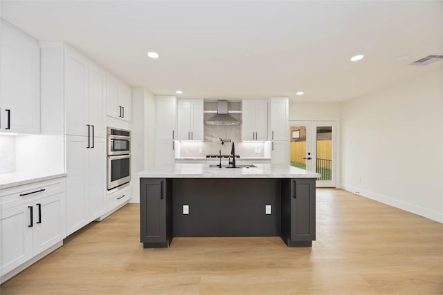 kitchen with double oven, visible vents, white cabinetry, and wall chimney exhaust hood